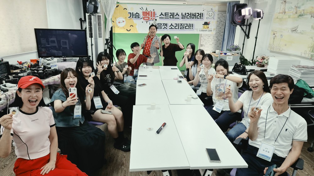 긴 테이블 양옆에 앉은 참가자들과 뒤편에 선 진행자들이 함께 웃으며 사진을 찍고 있다
