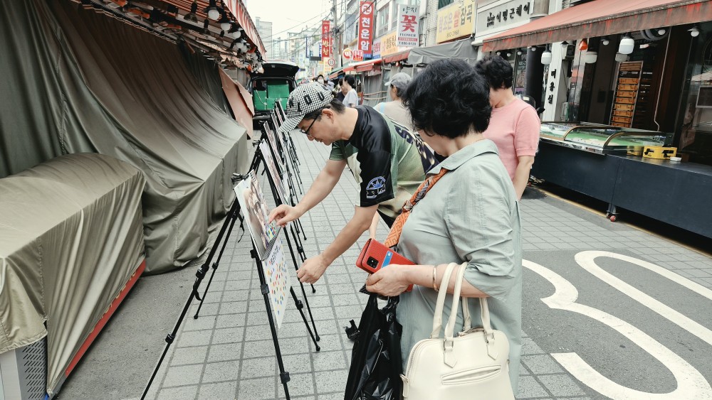 방문객 두 명이 이젤에 걸린 사진을 들여다보며 투표판을 살피고 있다